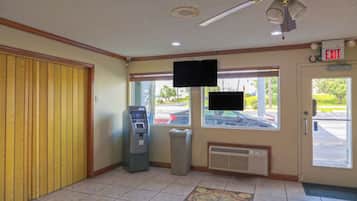 Un vestíbulo con panel de madera en la pared, un cajero automático, un televisor montado y una señal de salida.