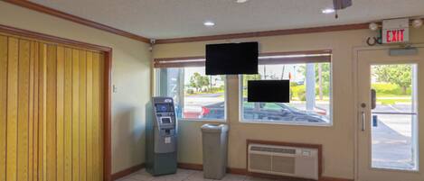 A lobby with a wooden panel wall, an ATM, a television mounted on the wall, and an exit sign.