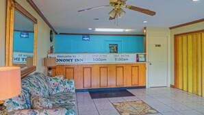 A reception area with a check-in/out desk, a sofa, a ceiling fan, and a welcome sign. - Economy Inn by OYO Ashburn I-75 (Ashburn)