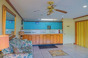A reception area with a check-in/out desk, a sofa, a ceiling fan, and a welcome sign. - Economy Inn by OYO Ashburn I-75 (Ashburn)
