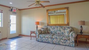 A room with a ceiling fan, a floral sofa, two lamps, a mirror, and a door with an exit sign. - Economy Inn Ashburn GA I-75 (Ashburn)
