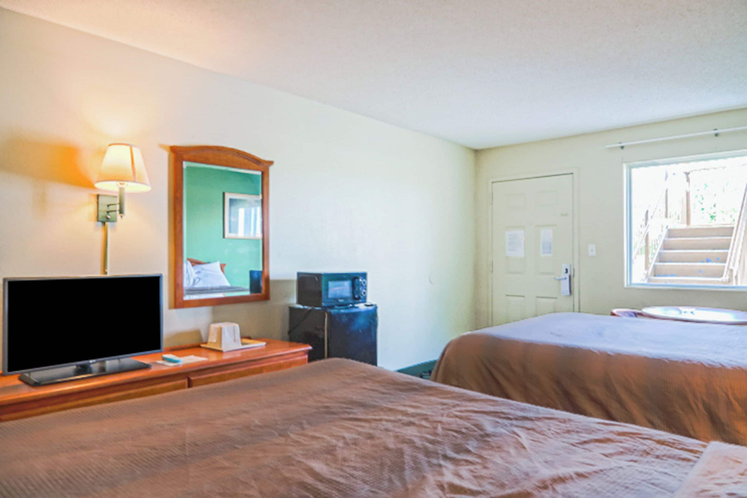 Une chambre d’hôtel avec deux lits, une télévision, une lampe, un four à micro-ondes et une fenêtre donnant sur un escalier.