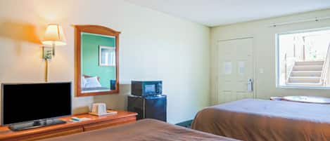 A hotel room with two beds, a television, a lamp, a microwave, and a window with a view of a staircase.