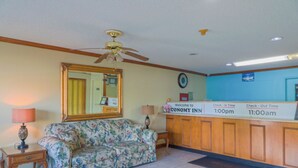 A reception area with a floral sofa, a wooden reception desk, a ceiling fan, and a clock on the wall. - Economy Inn Ashburn GA I-75 (Ashburn)