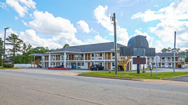 A motel with a large parking lot, a covered outdoor seating area, and a prominent dome-shaped building. - Economy Inn by OYO Ashburn I-75 (Ashburn)