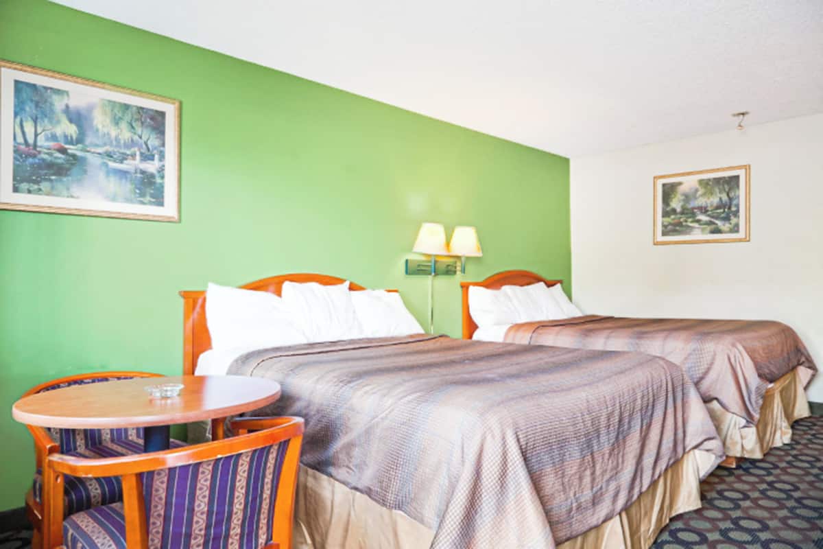 Habitación de hotel con dos camas, una mesa redonda de madera y dos sillas.