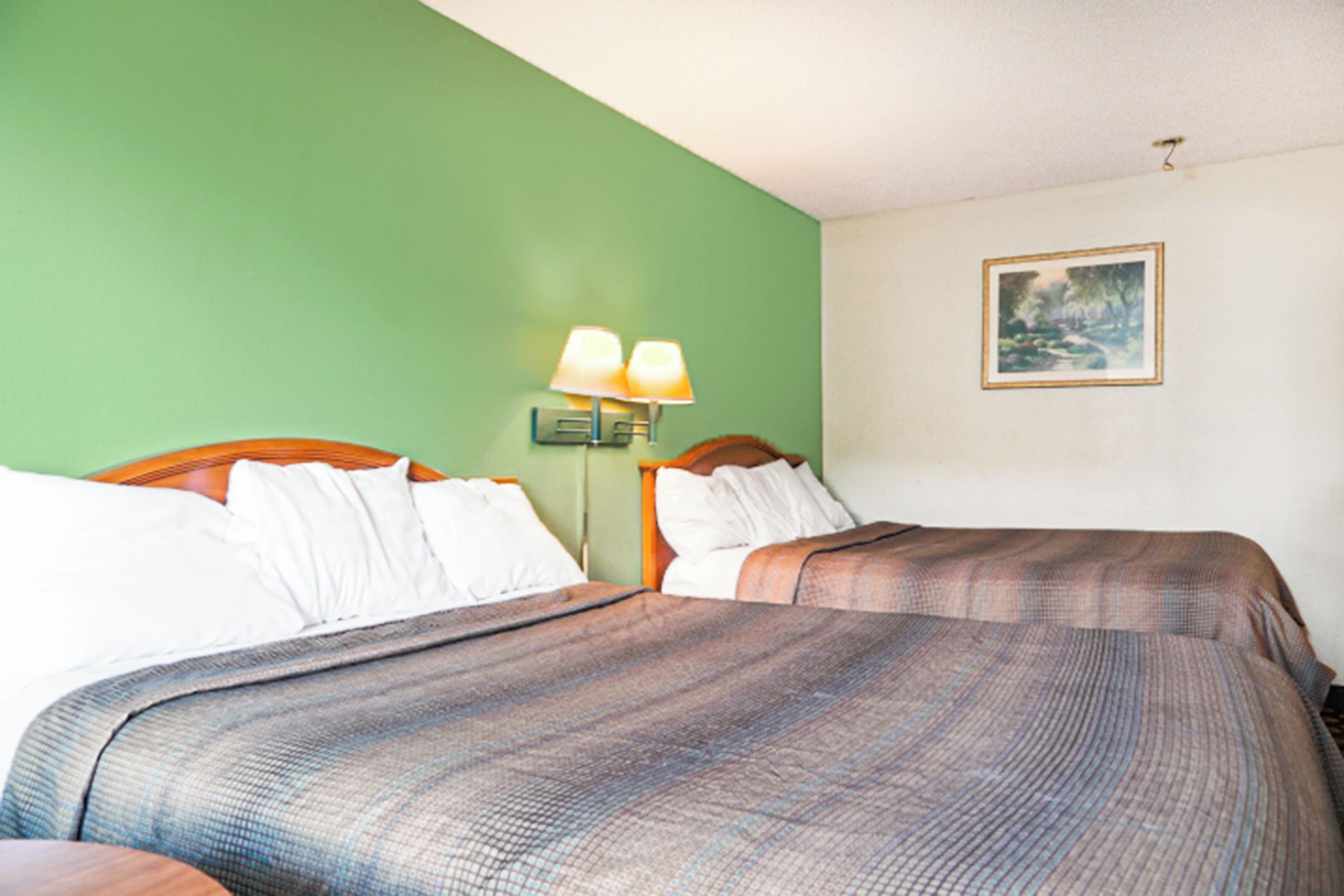 A hotel room with two beds, a green wall, a painting, and a nightstand with lamps.
