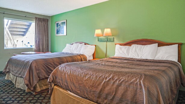 A hotel room with two beds, a window with curtains, a painting on the wall, and a nightstand with lamps. - Economy Inn Ashburn GA I-75 (Ashburn)