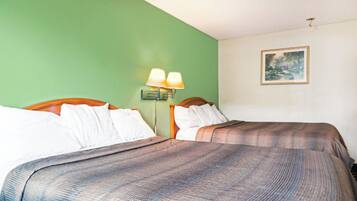 Una habitación de hotel con dos camas, una pared verde, un cuadro y una mesita de noche con lámparas.