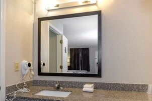Un baño con encimera de granito, un lavamanos blanco, un secador de pelo y un espejo.