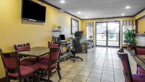Un comedor de hotel con varias mesas y sillas, un televisor de pantalla plana montado en la pared y vistas a través de puertas de vidrio.