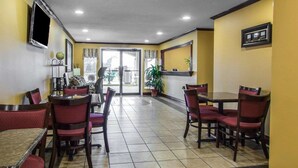 Un vestíbulo de hotel con suelo de baldosas, sillas tapizadas en rojo, un mostrador de recepción y un televisor montado en la pared.
