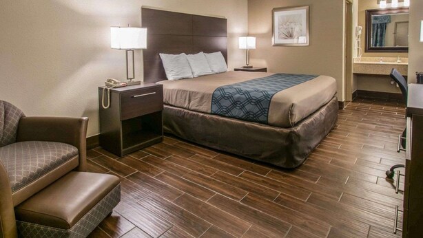 Una habitación de hotel con una cama, dos mesitas de noche con lámparas, una silla, un escritorio y un espejo.
