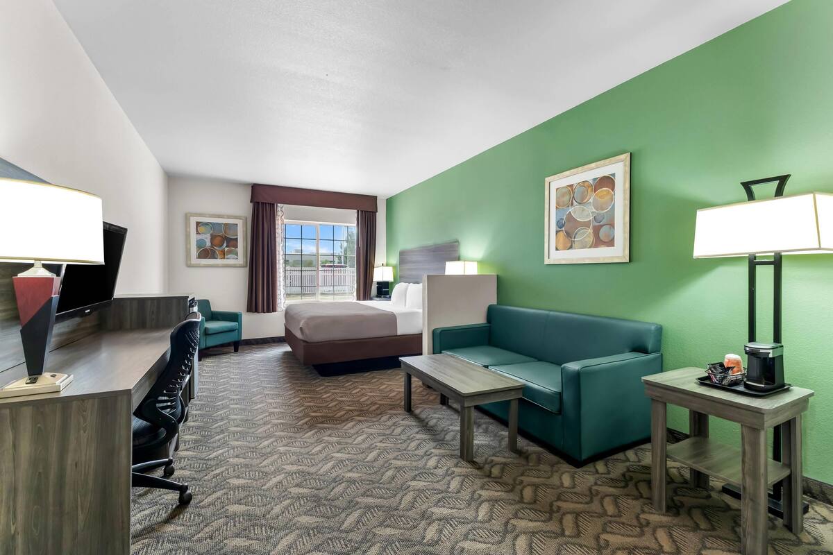 Une chambre d’hôtel avec un lit, un bureau avec un ordinateur, un canapé vert, une petite table et une lampe.