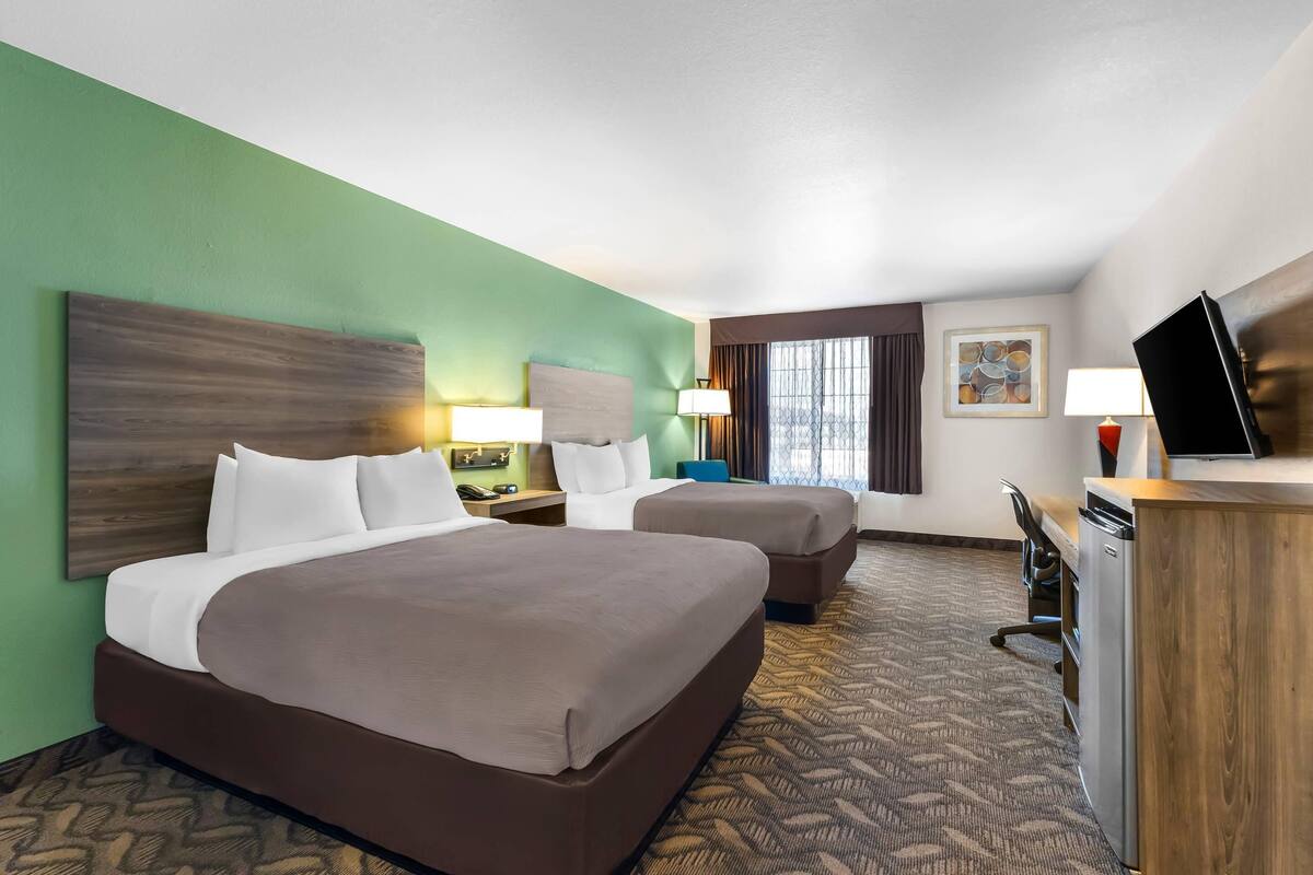 Une chambre d’hôtel avec deux lits, un bureau, une télévision et une fenêtre avec des rideaux.