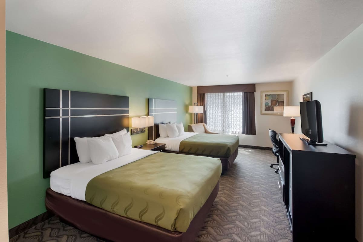 Une chambre d’hôtel avec deux lits, un bureau, une télévision et une fenêtre avec des rideaux.