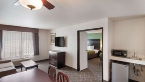 Une chambre d’hôtel comprenant une table à manger, des chaises, un téléviseur, une kitchenette et un lit situé dans la pièce adjacente.