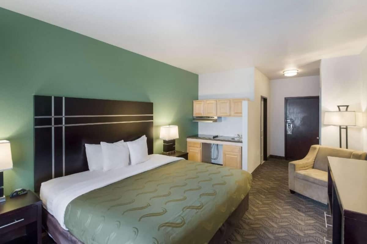 Een hotelkamer met een bed, een bureau, een stoel, een kitchenette en een deur.