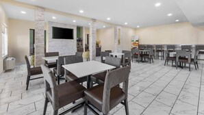 Un restaurant spacieux doté d’un sol en marbre, de nombreuses tables et chaises, d’un téléviseur à écran plat fixé au mur et d’un tableau affichant le menu.