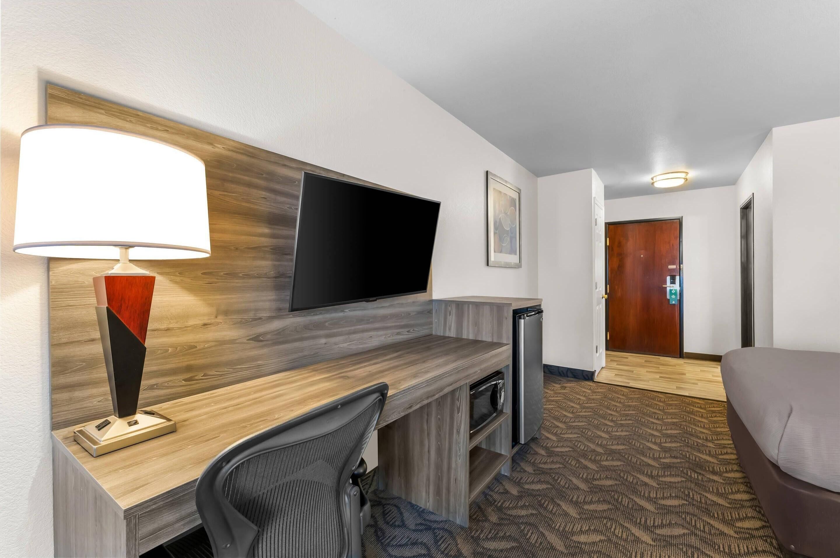 Ein Hotelzimmer mit einem Holztisch, einem Flachbildfernseher, einer Lampe, einem Stuhl, einem Bett und einem Teppichboden.