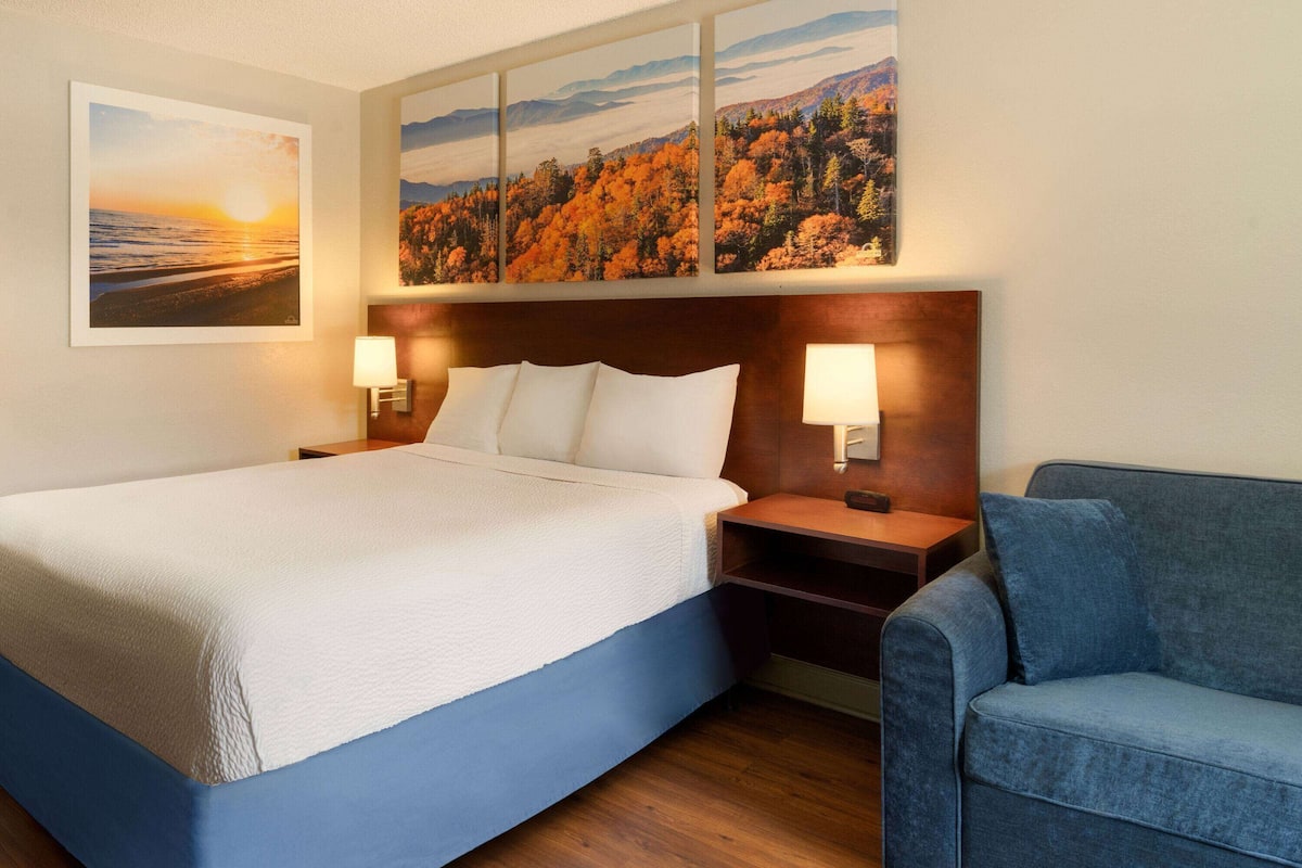 A hotel room with a large bed, two bedside tables with lamps, a blue sofa, and a wall with three framed pictures.