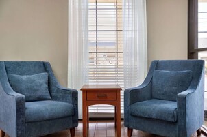 Two blue armchairs facing each other with a small wooden side table between them, in front of a window with blinds.