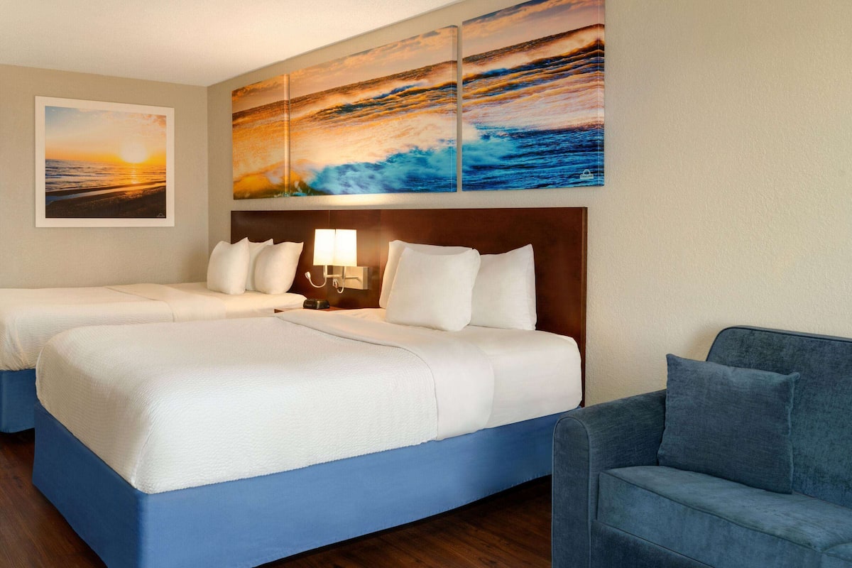 A hotel room with two beds, a blue couch, and a large painting of a sunset over the ocean.