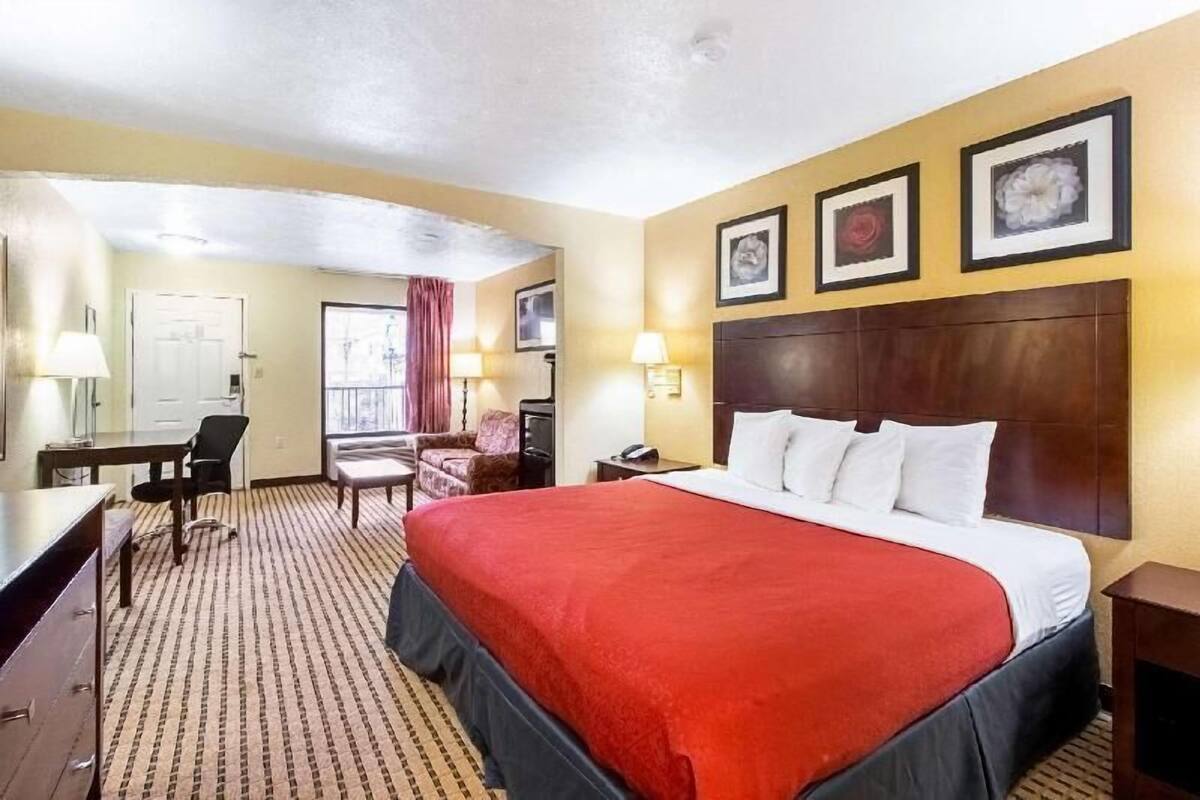 Une chambre d’hôtel avec un grand lit, un bureau, une chaise, une petite table et une fenêtre avec des rideaux.
