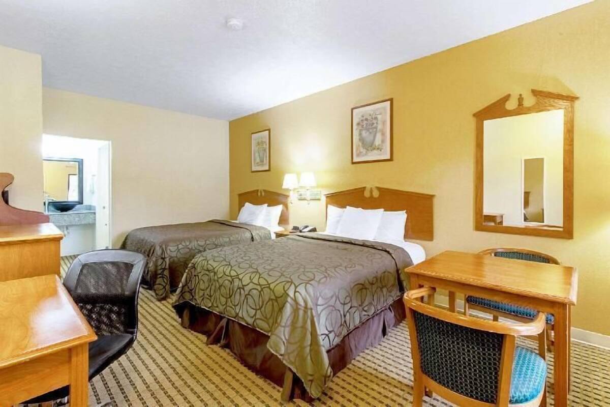 Une chambre d’hôtel avec deux lits, un bureau, une chaise, une table, un miroir et une porte.