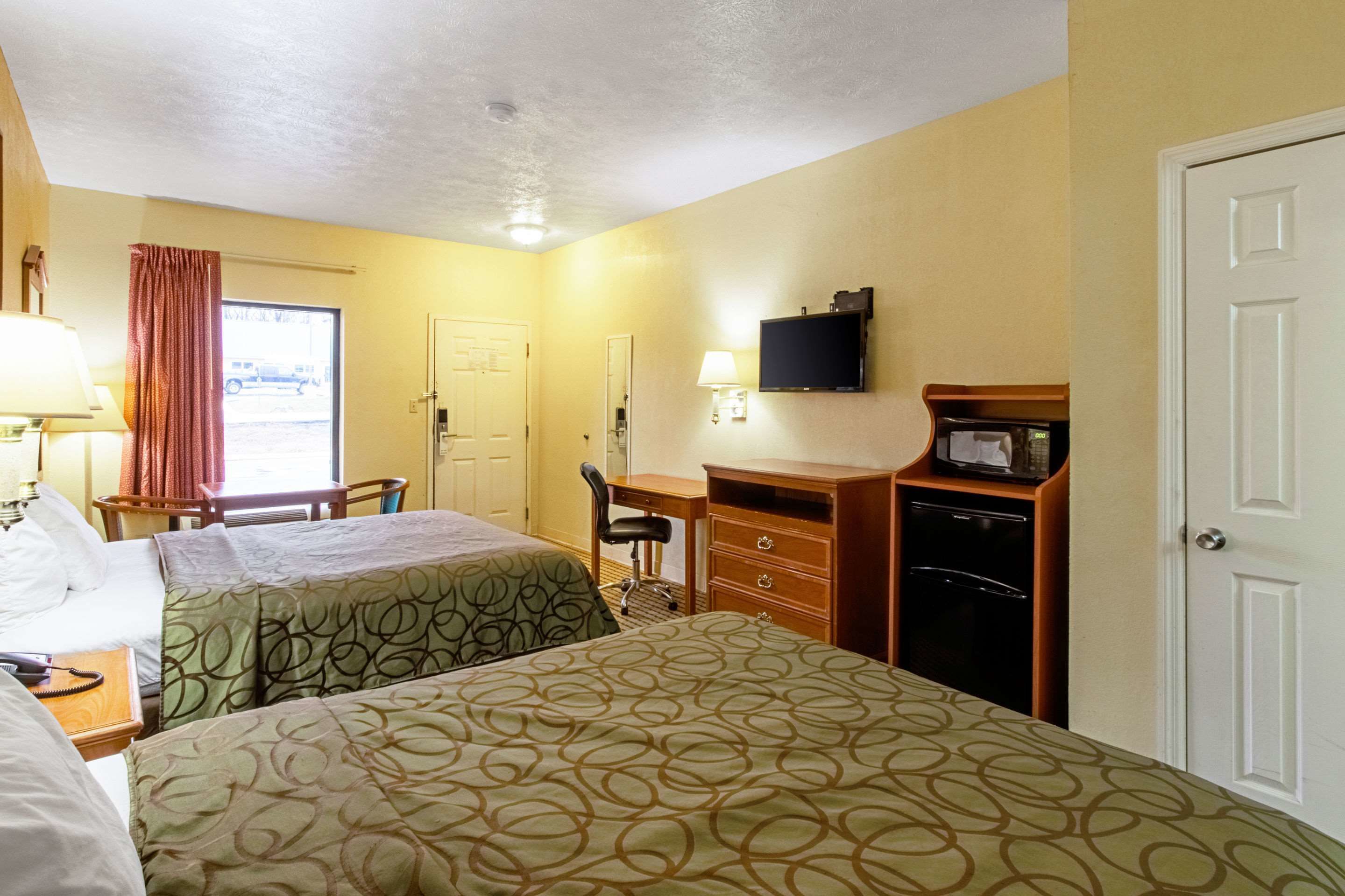 A hotel room with two beds, a desk, a chair, a television, a microwave, and a door.