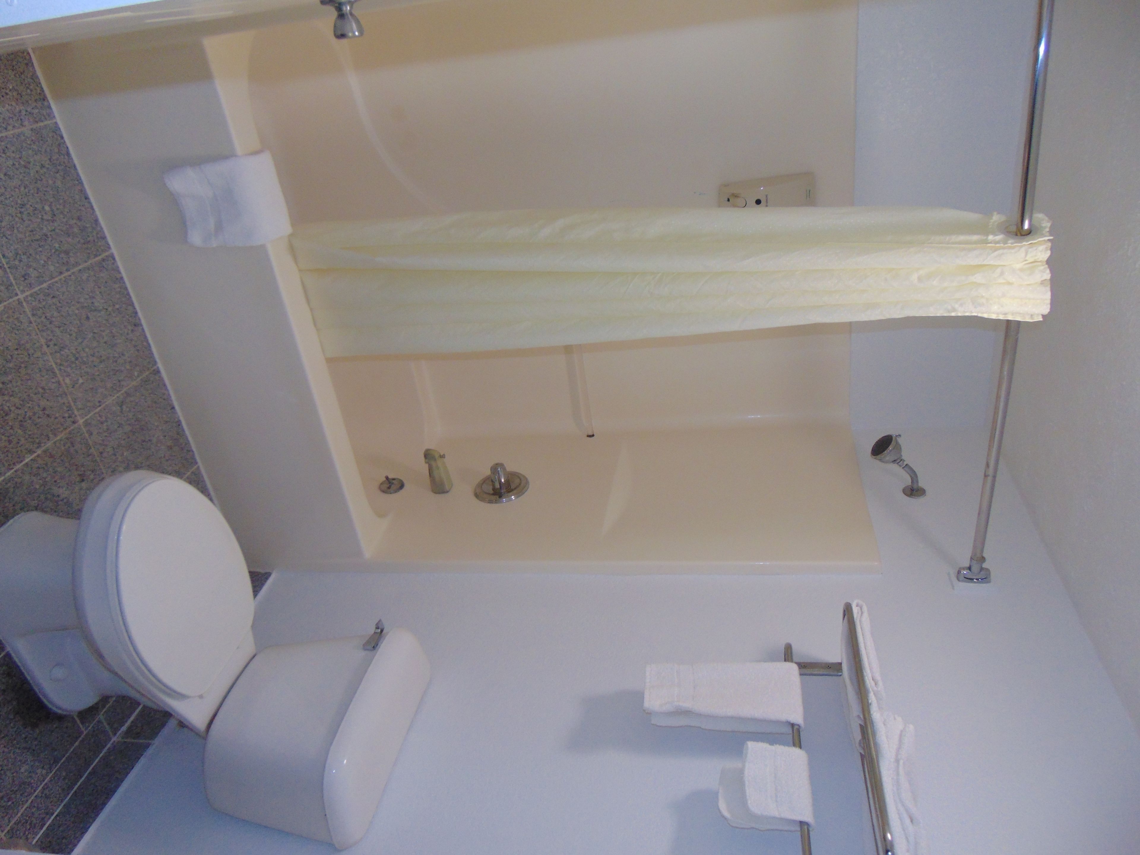 A bathroom with a bathtub, toilet, and handrails.