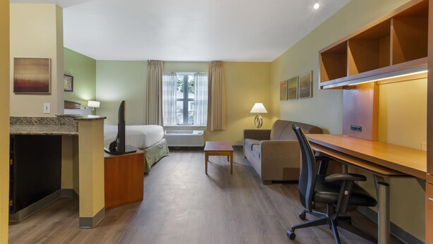 A hotel room with a bed, a desk, a chair, a lamp, a window with curtains, and a small table. - Extended Stay America Suites Atlanta Norcross Peachtree Corn (Norcross)