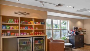 A kitchenette with shelves stocked with snacks and a refrigerator. There is a seating area with a chair and a small table. - Extended Stay America Suites Atlanta Norcross Peachtree Corn (Norcross)