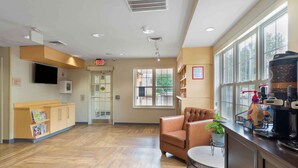 A spacious lobby with a wooden floor, a leather armchair, a coffee machine, and a large window with a view of the outside. - Extended Stay America Suites Atlanta Norcross Peachtree Corn (Norcross)