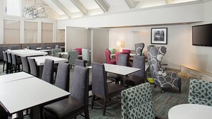 Une salle à manger d’hôtel avec plusieurs tables et chaises, un téléviseur fixé au mur et une moquette à motifs.