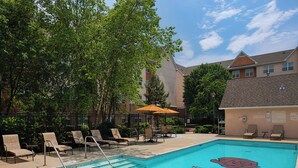 Une piscine entourée d’arbres et d’un bâtiment, avec des chaises longues et des parasols.