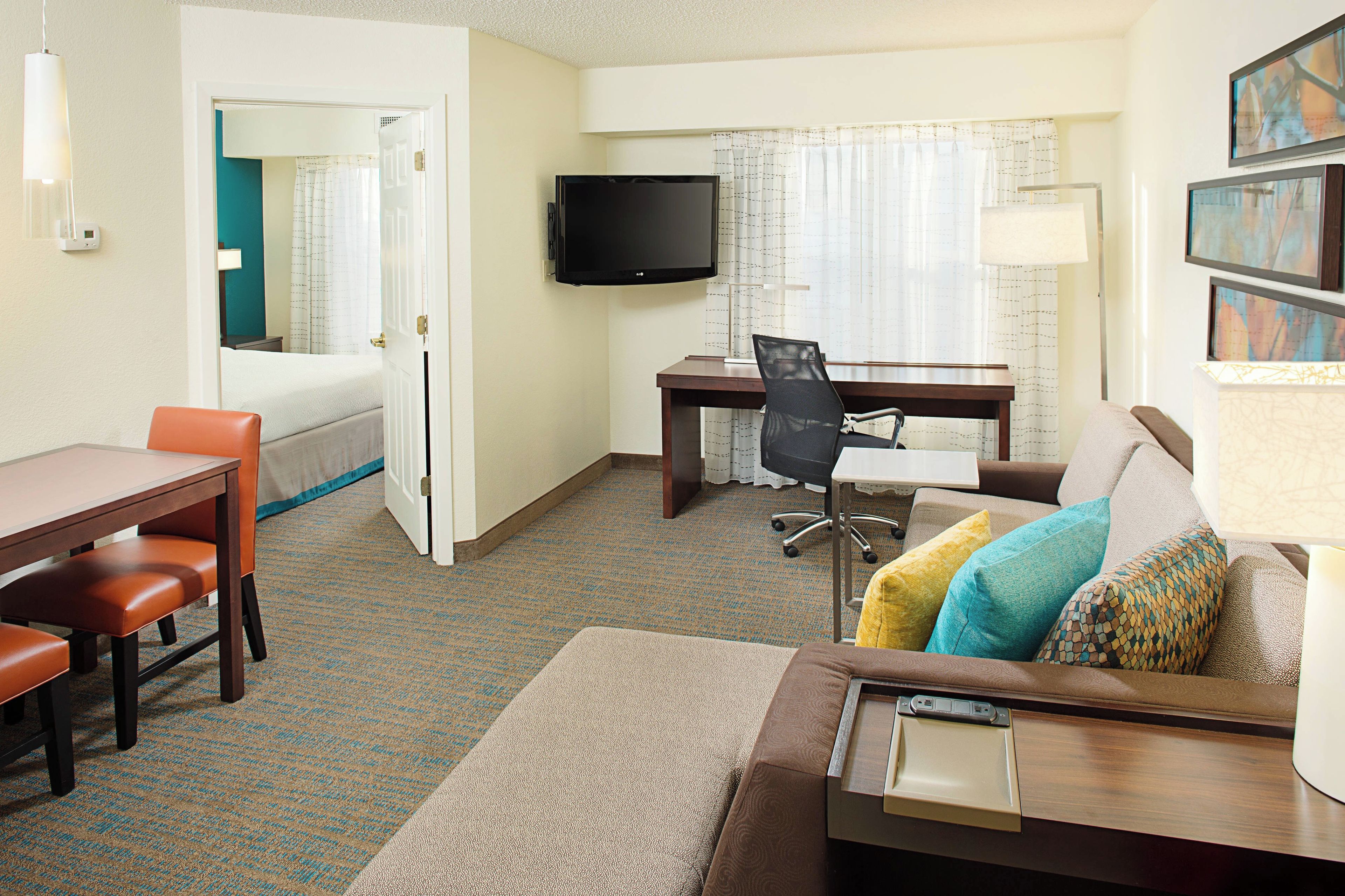 A hotel room with a bed, a desk with a chair, a television, and a sofa with cushions.