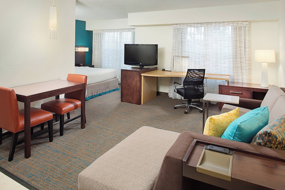 A hotel room with a bed, desk, chair, television, and a sofa with a tray table.