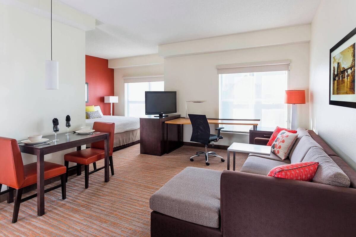 Ein Hotelzimmer mit Bett, Schreibtisch, Fernseher, einer Sitzecke und einem Essbereich mit Stühlen und Tisch.