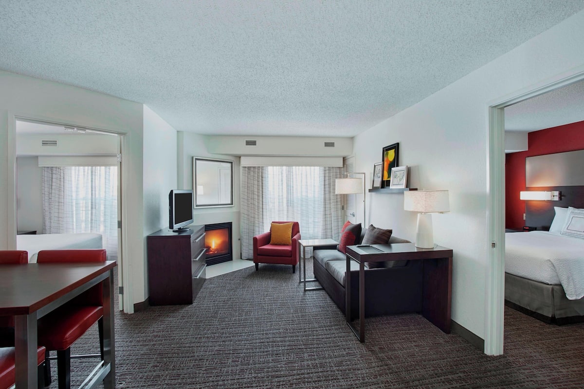 A hotel room with a bed, a desk, a chair, a TV, and a fireplace.