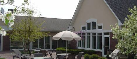 An outdoor patio area with tables and chairs, a grill, and a building with large windows.