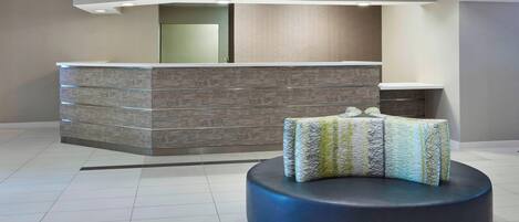 A reception area with a modern design, featuring a reception desk, a seating area with a patterned ottoman, and a decorative light fixture.