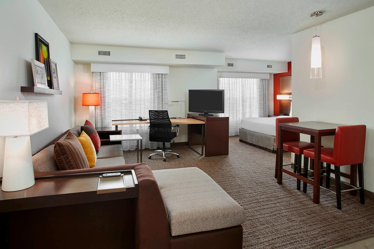 A hotel room with a sofa, a desk, a TV, a bed, and a small dining area.
