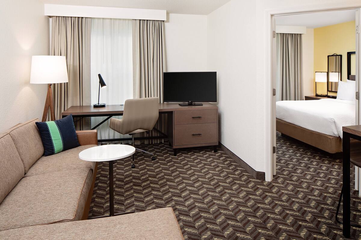 A hotel room with a sofa, a desk with a computer, a bed, and a mirror.