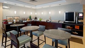 A modern hotel kitchen with granite countertops, a large TV, and a self-service breakfast bar.