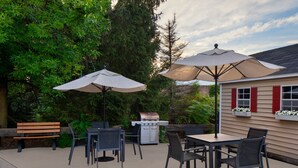 Eine Terrasse im Freien mit Grill, Tischen, Stühlen und Sonnenschirmen.