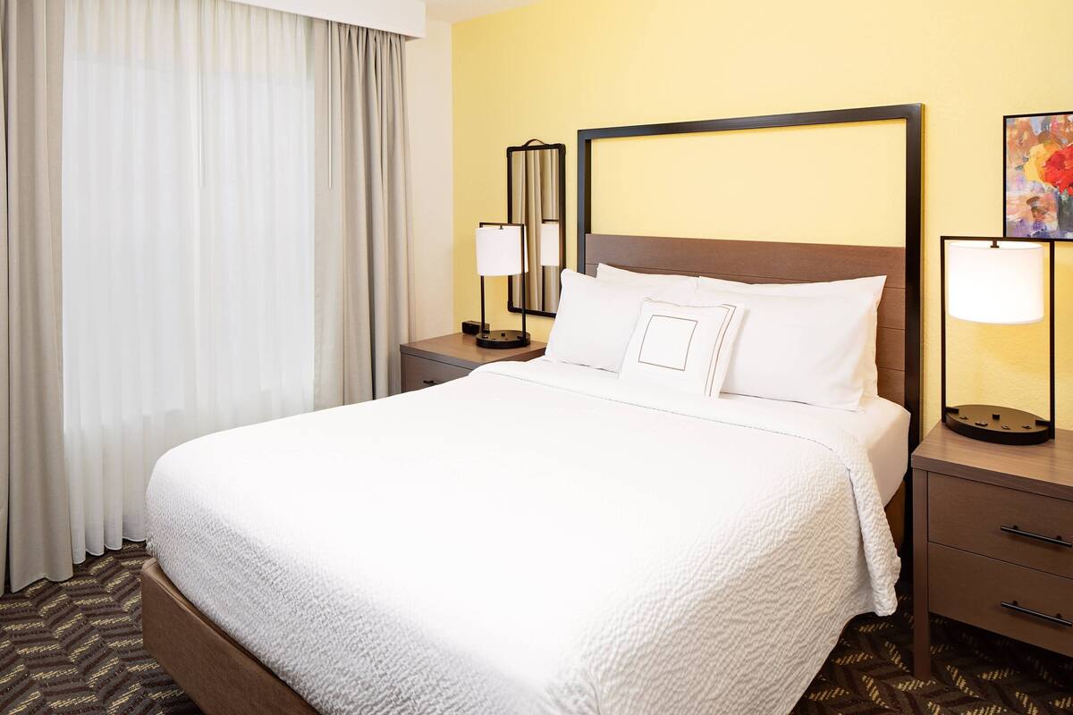 A hotel room with a large bed, a nightstand with a lamp, and a painting on the wall.