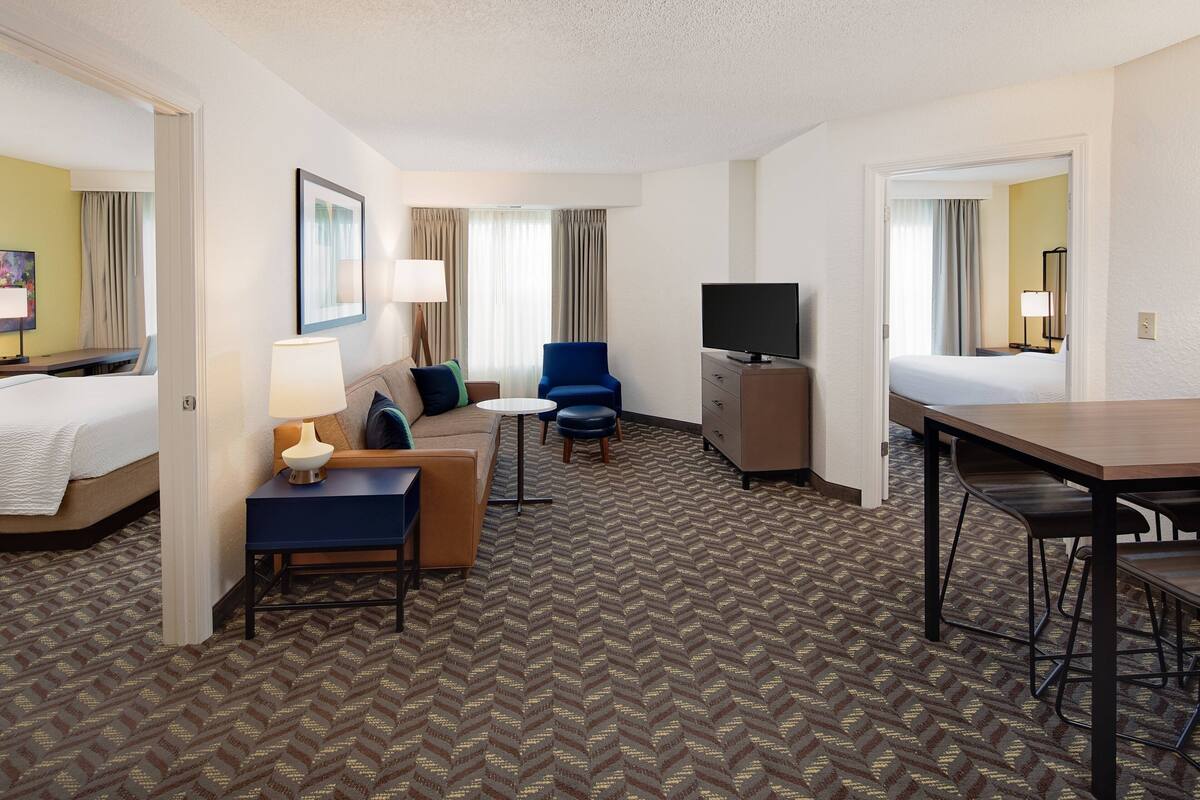 A hotel room with a bed, a desk, a chair, a sofa, a television, and a patterned carpet.