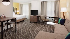 A hotel room with a bed, desk, chair, sofa, and a television.
