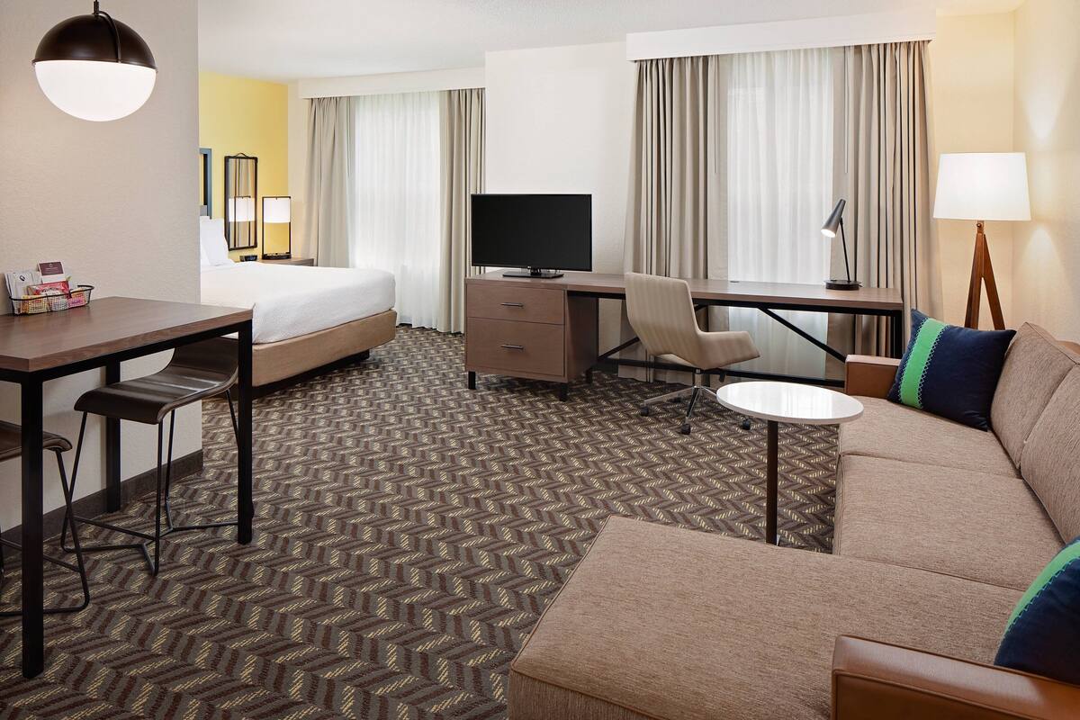 A hotel room with a bed, desk, chair, sofa, and a television.